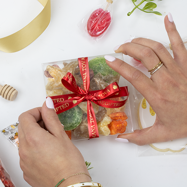 Hands Holding a Rosh Hashana Box of Tropical Dried Fruit with Red & Gold Ribbon