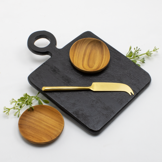 Black mango wood cutting and serving board, gold cheese knife and 2 acacia pinch bowls on a white background