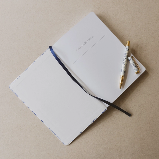 Open blue floral journal with a matching blue floral and gold pen on a beige background