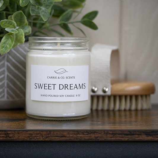 The Blissful Spa Gift Box featuring a white magnetic gift box, waffle weave robe, sweet dreams scented candles, bath salts, hand cream, bath brush, candle wick cutter, matches with gold embossed box, lavender scented body roll on, and faux plant in stone holder.