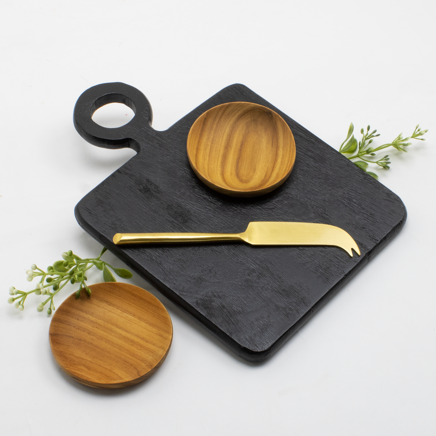 Black mango wood cutting and serving board, gold cheese knife and 2 acacia pinch bowls on a white background