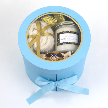 Gift set with a candle, cozy socks, and matchbox in a blue round gift box on a white background